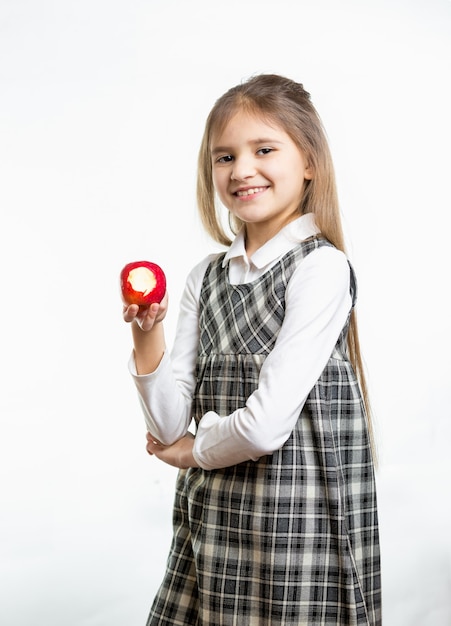 Na białym tle portret szczęśliwej dziewczyny w szkolnym mundurku trzyma czerwone jabłko