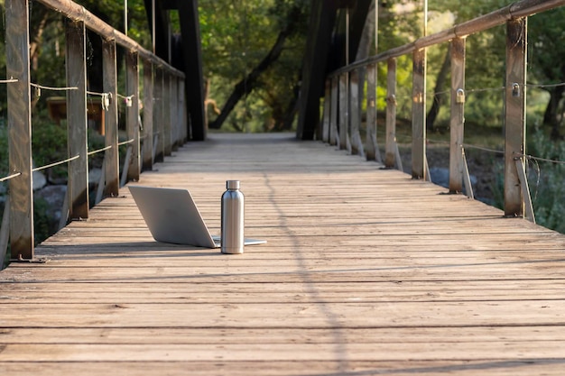 Na białym tle widok z przodu laptopa i metalowej butelki wody na drewnianej podłodze z naturą w tle i kopią przestrzeni