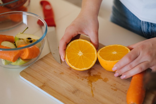 Na drewnianym stole nacięte pomarańcze. Ręce kobiety trzymają dwa kawałki owoców.