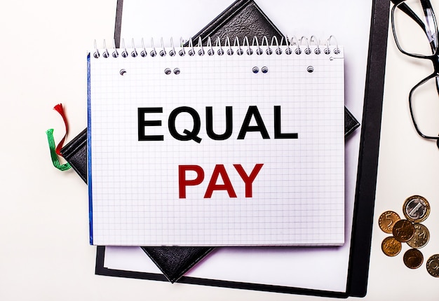 Na jasnej powierzchni szklanki, monety i notes z napisem EQUAL PAY. Pomysł na biznes.