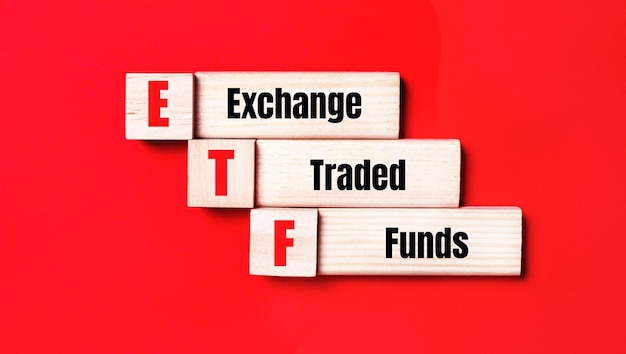 Na jasnoczerwonym tle drewniane kostki i klocki z napisem ETF Exchange Traded Funds Produkcja zabawek drewnianych