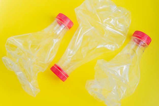 Na jasnożółtym tle leżały płasko trzy zgniecione plastikowe butelki. Brak koncepcji odpadów i recyklingu