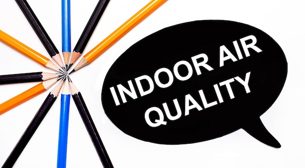 Na jasnym tle kolorowe kredki, a na czarnym tle biała kartka z napisem INDOOR AIR QUALITY