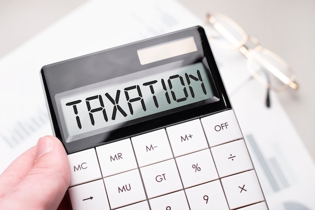 Zdjęcie na kalkulatorze widnieje napis taxation. biznes człowiek trzyma kalkulator w ręku.