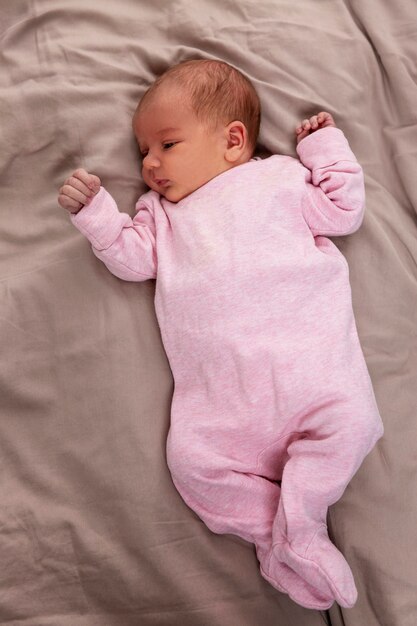 Zdjęcie na łóżku leży niemowlę w różowym ubraniu. miłość i czułość. pionowy.