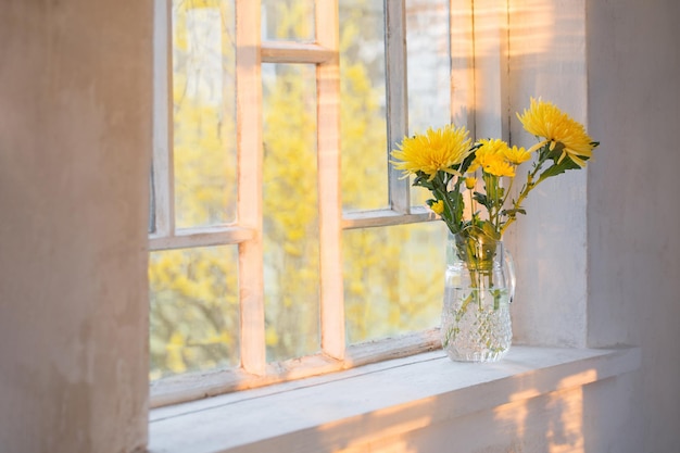Na parapecie stoi wazon z żółtymi kwiatami.