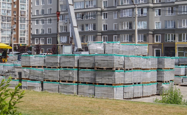 Na placu budowy jest wiele nowych szarych płyt chodnikowych na paletach pokrytych tworzywem sztucznym. Nawierzchnia chodników dla pieszych na ulicy miasta. Pierwszoplanowy. Remont chodnika na rynku miejskim.