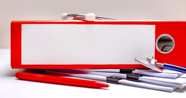 Na pulpicie stetoskop, długopis, czerwona teczka z plikami z miejscem na wstawienie tekstu. Koncepcja medyczna