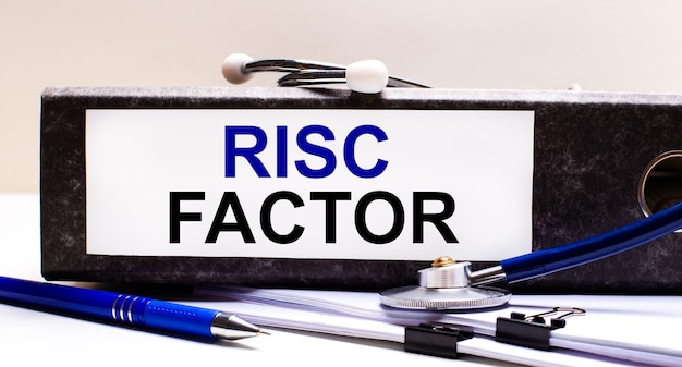Na pulpicie znajduje się stetoskop, niebieski długopis i szara teczka z tekstem RISK FACTOR. Koncepcja medyczna