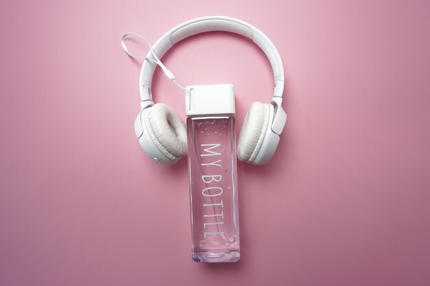 Na różowym tle jest butelka wody i słuchawki