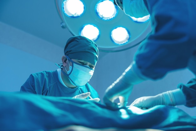 Na sali operacyjnej szpitala grupa chirurgów przeprowadza operację Na sali operacyjnej kliniki chirurgicznej chirurgii żylnej naczyń azjatycki lekarz i asystent