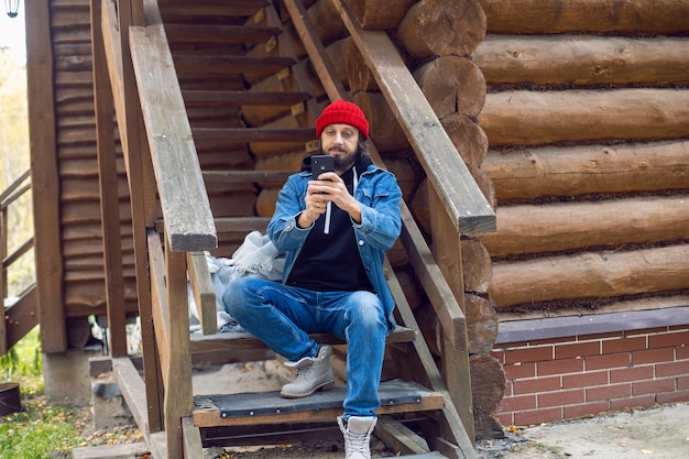 Na schodach siedzi mężczyzna z hipsterską brodą w czerwonej czapce z dzianiny i dżinsowej kurtce