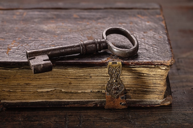 Na starej księdze z zapięciami znajduje się stary klucz wykonany z metalu Antyczne przedmioty na ciemnym drewnianym odwrocie