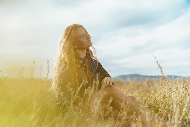 Na stepie na tle nieba siedzi uśmiechnięta blond dziewczyna naturalne piękno