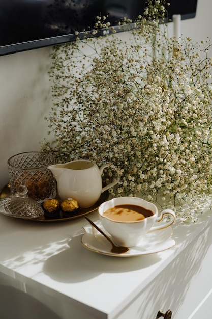 Zdjęcie na stole bukiet kwiatów, filiżanka herbaty lub kawy z mlekiem i słodyczami.