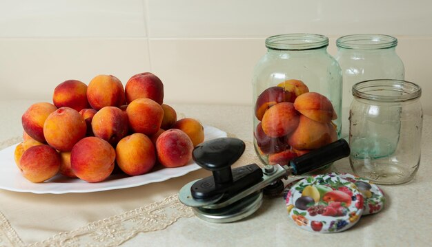 Zdjęcie na stole naczynie z brzoskwiniami słoiki do domowego konserwowania pokrywek do słoików i klucz do konserw