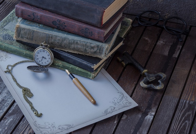 Zdjęcie na stole są stare książki, zegarki kieszonkowe, wieczne pióro, szklanki i papier do pisania