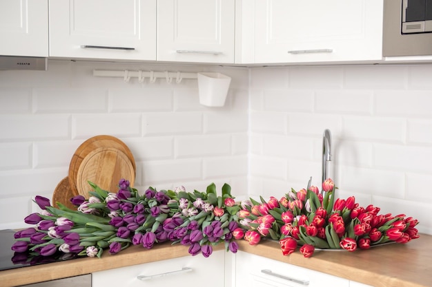 Na stole w kuchni leży duża liczba tulipanów w różnych kolorach. Kwiaty w zlewie