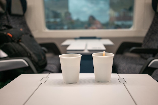 Na stole w pociągu leżą dwie białe jednorazowe filiżanki kawy