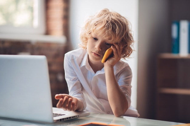 Na telefonie. Ładny blond chłopiec siedzi i rozmawia przez telefon