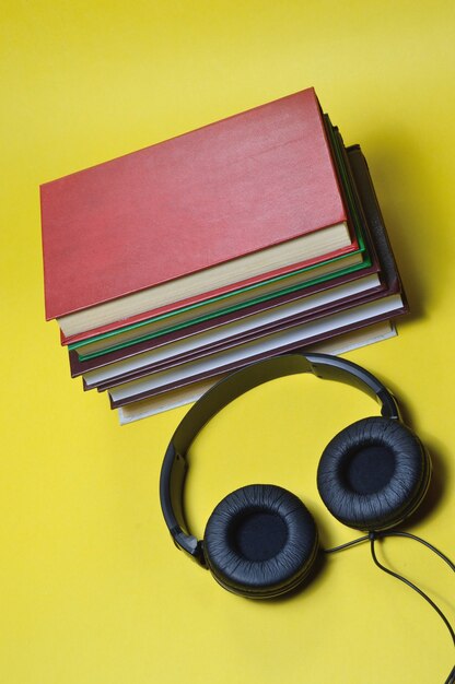 na żółtym tle stos książek i duże, czarne słuchawki.