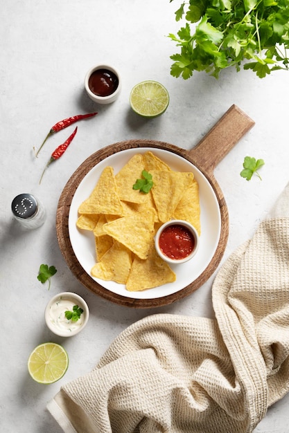 Nachos z chipsami kukurydzianymi z salsą i sosem serowym, świeżymi ziołami, limonką i papryczką chili na białym tle. Koncepcja kuchni meksykańskiej. Widok z góry i miejsce na kopię.