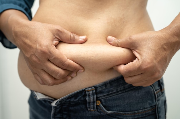 Zdjęcie nadwaga azjatka pokazuje i używa ręki do ściśnięcia tłuszczu brzucha
