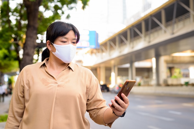 Nadwaga azjatycka kobieta z maską w celu ochrony przed epidemią wirusa korony za pomocą telefonu na ulicy na zewnątrz