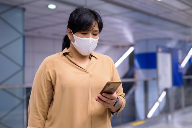 Nadwaga azjatyckie kobiety za pomocą telefonu z maską w celu ochrony przed epidemią wirusa koronowego na stacji metra
