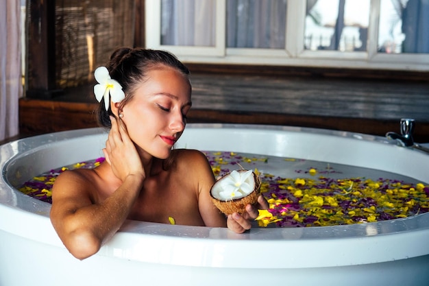 Naga brunetka młoda kobieta relaksuje się w kąpieli z płatkami w tropikach Czas dla siebieromantyczny 14 lutego walentynki w salonie spa eko hoteleletnie wakacje w tropikalnym raju na plaży
