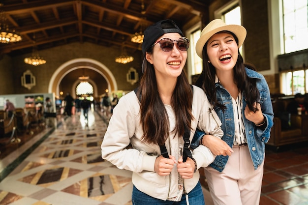 najlepsi przyjaciele radośnie spacerują ramię w ramię na stacji kolejowej w Los Angeles. dwie siostry spacerujące po sali klasycznego budynku. podróż z koncepcją przyjaciół.