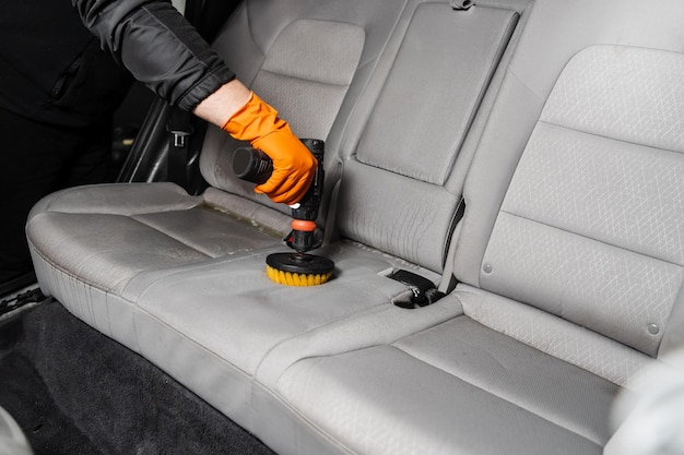 Nakładanie detergentu na tekstylne siedzenie we wnętrzu samochodu do czyszczenia na sucho Rozmazywanie detergentu na tekstylnych siedzeniach samochodowych za pomocą wiertarki ze szczotką do czyszczenia na sucho