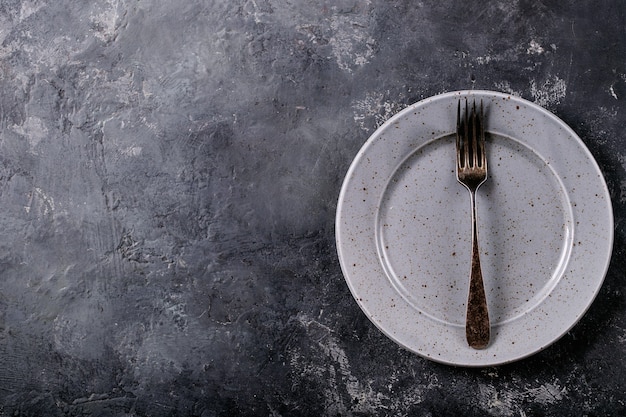 Zdjęcie nakrycie kolacji. nowoczesna niebieska płyta ceramiczna ze srebrnym widelcem na powierzchni o ciemnej teksturze. widok z góry, płaski układ.