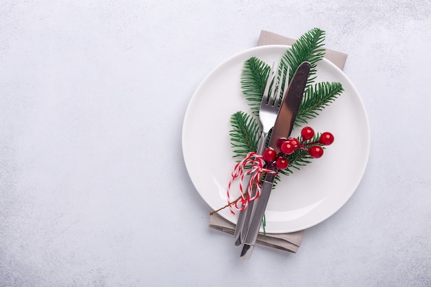 Nakrycie świątecznego stołu z pustym białym talerzem, cukierkami, gałęzią jodły i sztućcami z świątecznymi dekoracjami na kamiennym tle - obraz