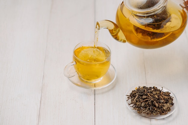 Nalewanie Herbaty. Filiżanka Gorącej Herbaty I Liści Herbaty Na Drewnianym Stole
