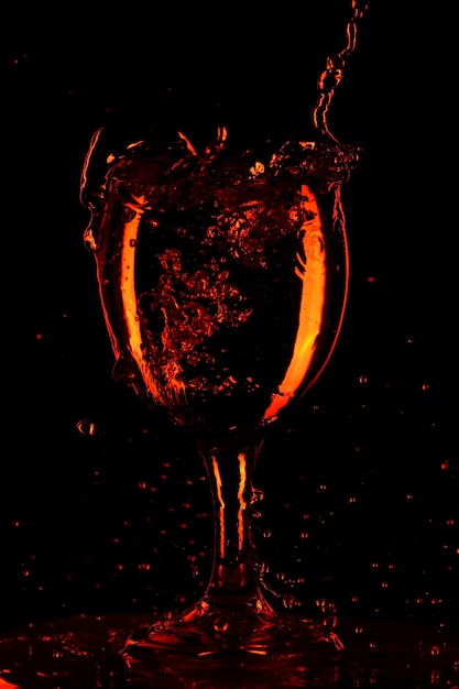 Zdjęcie nalewanie wody do szklanki na czarnym tle. pomarańczowa woda w szklance