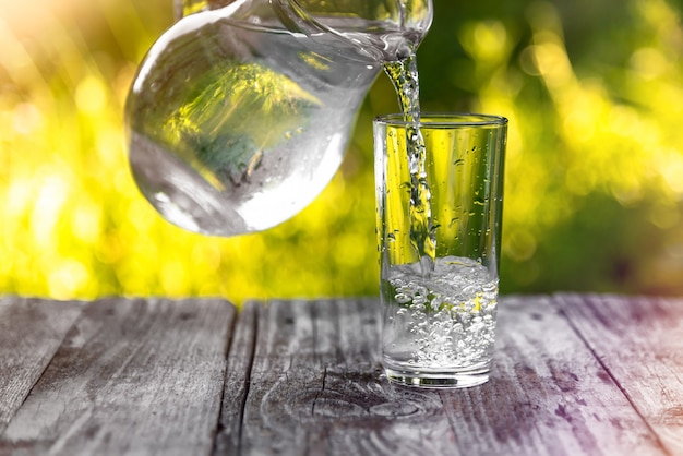 Nalewanie wody do szklanki ze szklanej karafki na tle zielonej natury.