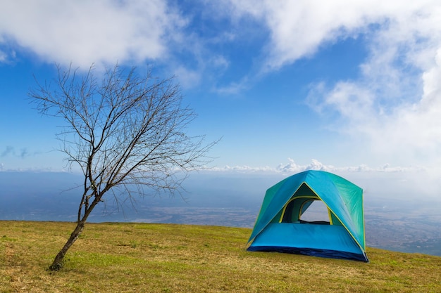 Namiot biwakowy na trawie pod białymi chmurami i błękitnym niebem w godzinach porannych