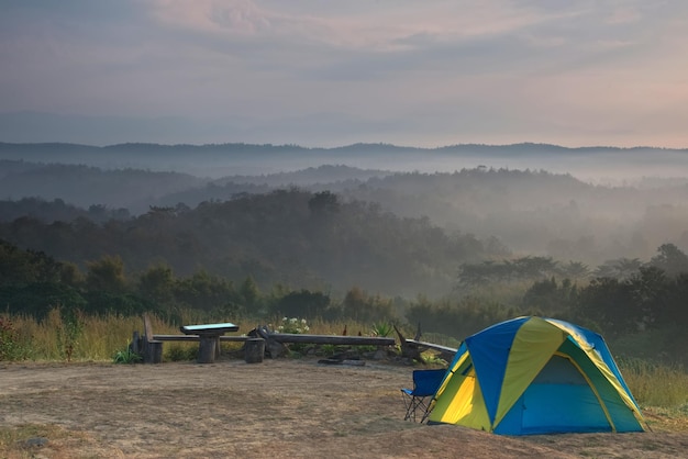 Namiot na kolorowym polu trawy z mglistym wzgórzem i wschodem słońca w tle
