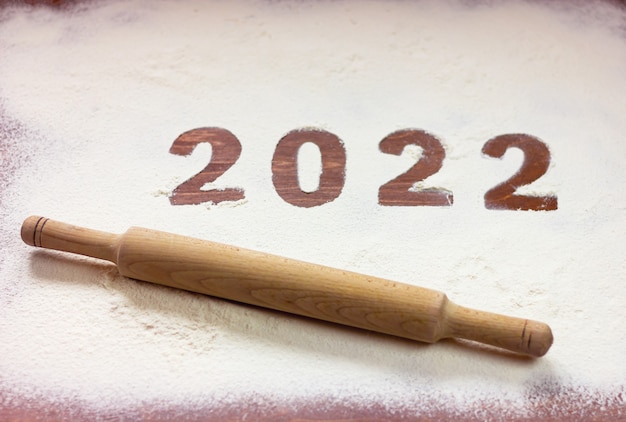 Napis 2022 wypisany jest na mące na drewnianym stole, a obok niego wałek do ciasta. koncepcja nowego roku.