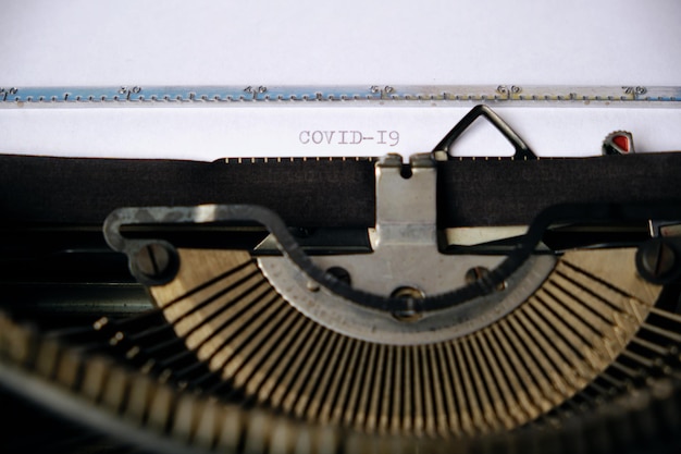 Napis COVID-19 jest wydrukowany na białej kartce ze starej maszyny do pisania.