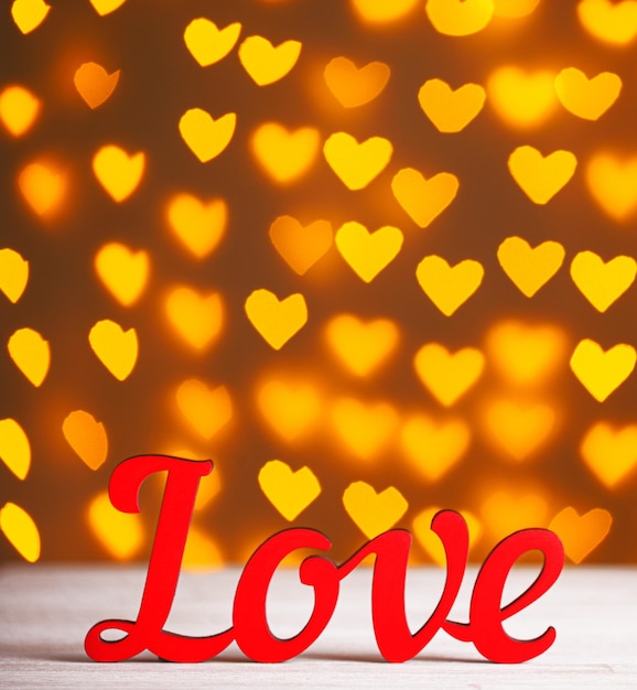 Napis Love na drewnianym tle z pięknymi sercami wykonanymi ze świateł na rozmytym tle