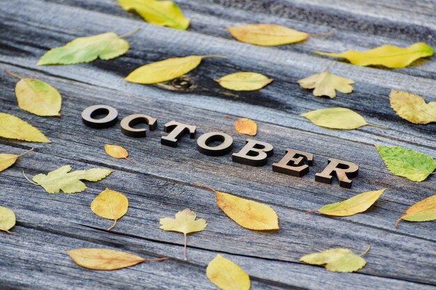 Zdjęcie napis października na drewnianej desce z żółtymi liśćmi