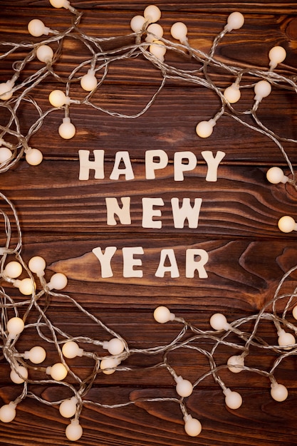 Zdjęcie napis szczęśliwego nowego roku, wieniec lampek choinkowych na ciemnym rustykalnym drewnianym stole.