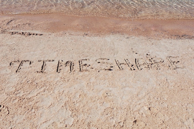 Napis "TimeShare" na piasku na plaży.