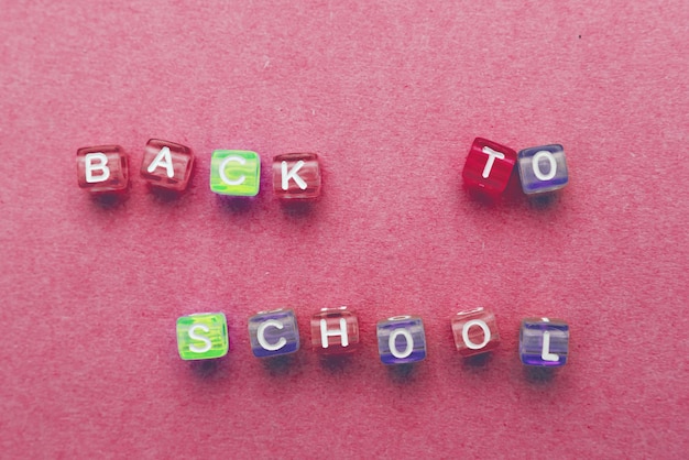 Napis z powrotem do szkoły wykonany przez wielokolorowe plastikowe kostki na czerwonym różowym tle