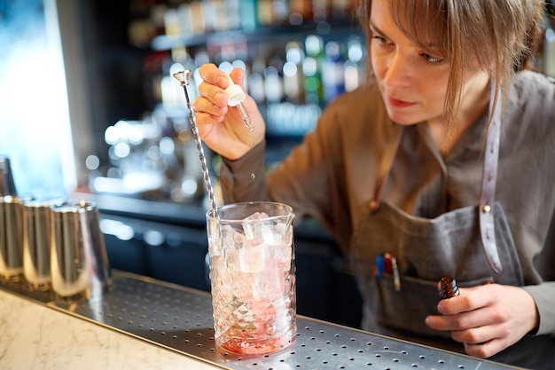 napoje alkoholowe, ludzie i koncepcja luksusu - barmanka przygotowuje koktajl i dodaje esencję do szklanki z lodem przy barze