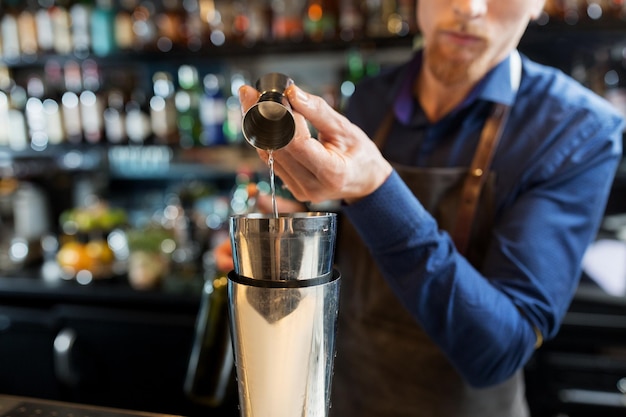 napoje, ludzie i luksus - barman nalewa alkohol z jigger do shaker i przygotowuje koktajl w barze