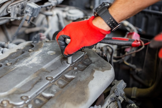 Zdjęcie naprawa samochodu mechanik samochodowy odkręca pokrywę mechanizmu dystrybucji gazu kluczem szczelinowym