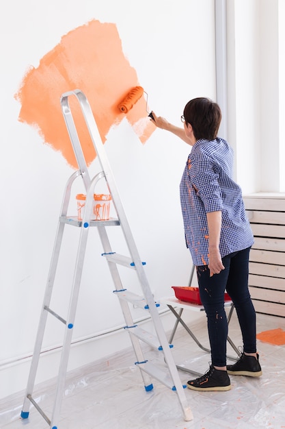 Naprawa w mieszkaniu. Szczęśliwa kobieta w średnim wieku maluje ścianę farbą.